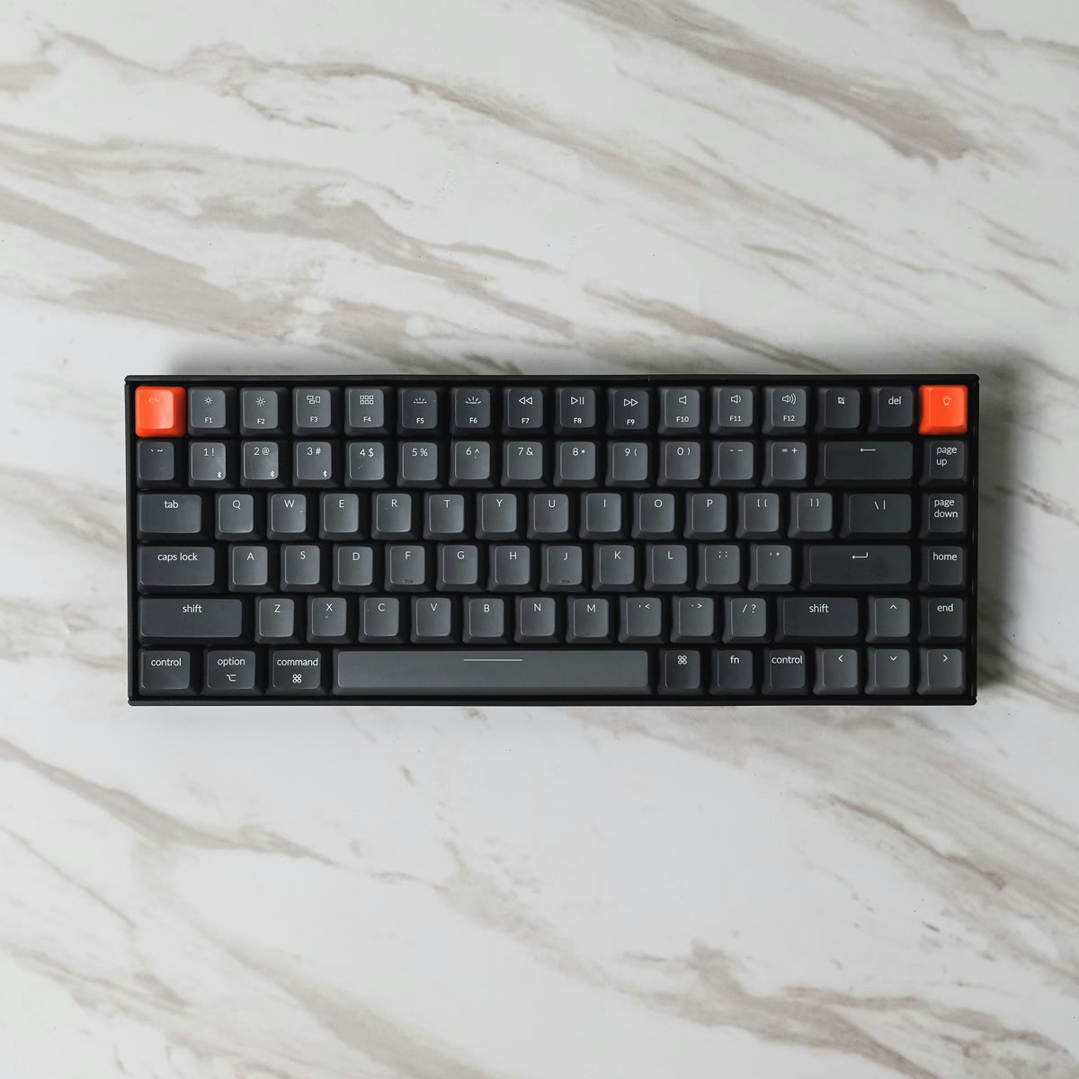 Mechanical keyboard with dark gray keys and orange accents on white marble